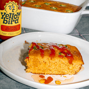 A slice of cornbread drizzled with Yellowbird Jalapeño Hot Sauce